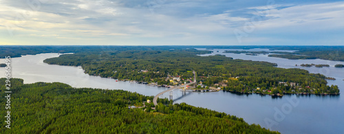 Aerial view on the bridge over the lake and trees in the forest on the shore. Blue lakes, islands and green forests from above on a cloudy summer day. Lake landscape in Finland, Puumala.