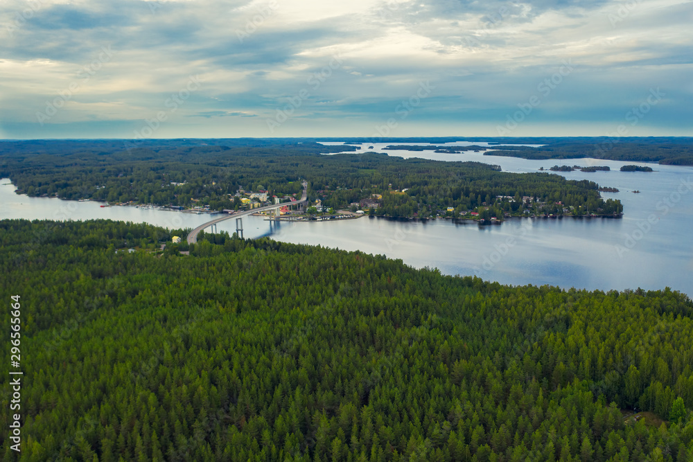 Aerial view on the bridge over the lake and trees in the forest on the shore. Blue lakes, islands and green forests from above on a cloudy summer day. Lake landscape in Finland, Puumala.