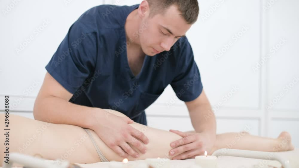 Close-up of a male physiotherapist doing a light massage to warm up the hips and buttocks of a young woman in a professional spa salon next to a sprig of cotton. 4K massage body care concept Close-up of a male physiotherapist doing a light massage to warm up the hips and buttocks of a young woman in a professional spa salon next to a sprig of cotton. 4K massage body care concept