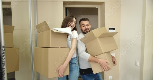 Happy young male and woman entering new apartment with cardboard boxes, laughing and having fun, new life beginning