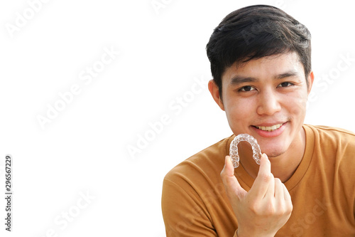 close up (isolated) young asian man smiling with hand holding dental aligner retainer (invisible) on white background of dental clinic for beautiful teeth treatment course concept