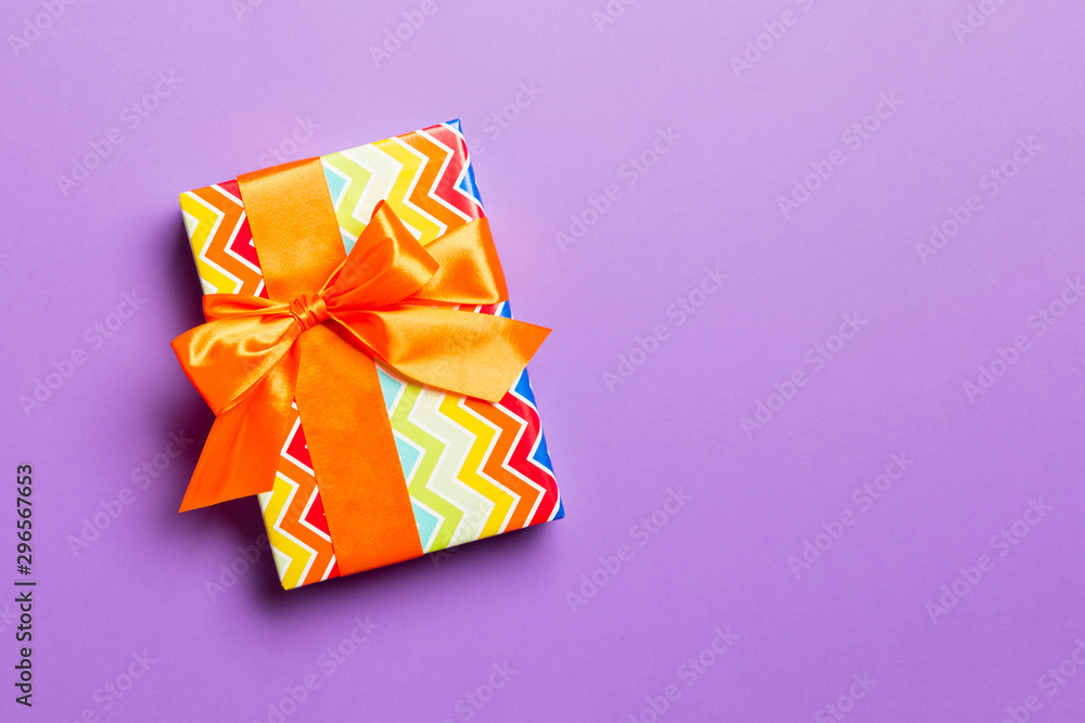 Gift box with orange bow for Christmas or New Year day on purple background, top view with copy space Gift box with orange bow for Christmas or New Year day on purple background, top view with copy space