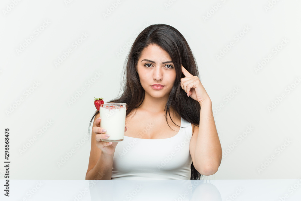 Young hispanic woman holding a smoothie young hispanic woman holding an avocado toast pointing his temple with finger, thinking, focused on a task.< mixto > Young hispanic woman holding a smoothie young hispanic woman holding an avocado toast pointing his temple with finger, thinking, focused on a task.< mixto >