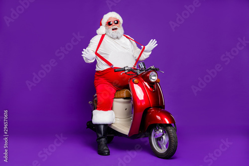 Photo of grey hair santa claus man came newyear theme party by bike cool stylish look wear sun spectacles trousers hat red suspenders isolated purple background
