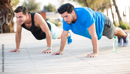 Smiling adult men are doing push-ups