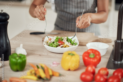 Close up of mixed race woman in apron mixing vegetables in bowl while standing in kitchen at home.