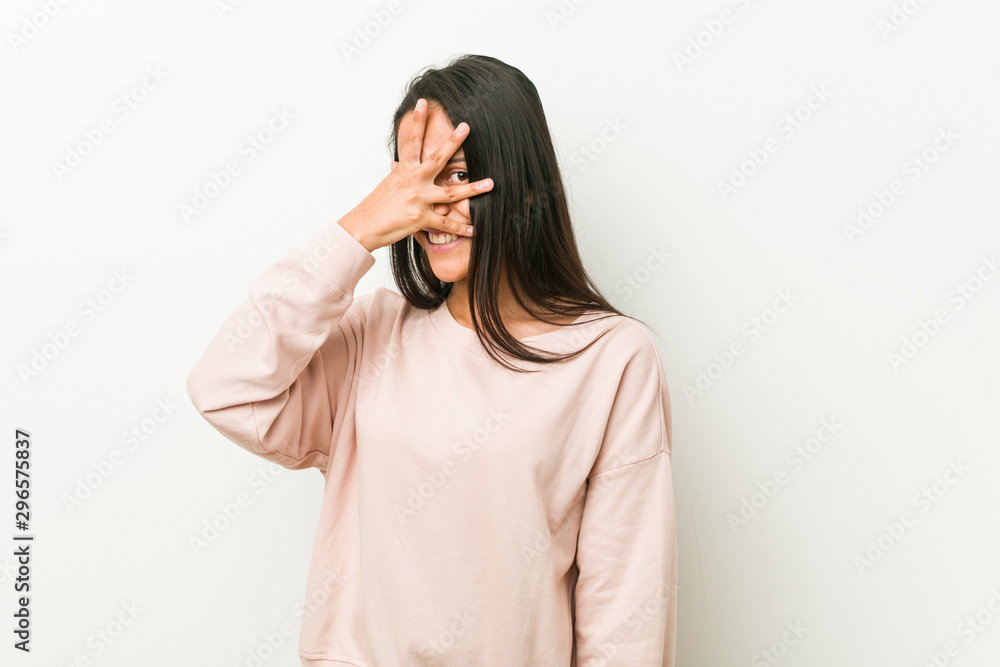 Young cute hispanic teenager woman blink at the camera through fingers, embarrassed covering face. Young cute hispanic teenager woman blink at the camera through fingers, embarrassed covering face.