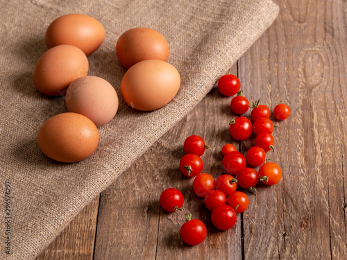 Chicken eggs and cherry tomatoes lie on bags on wooden boards.