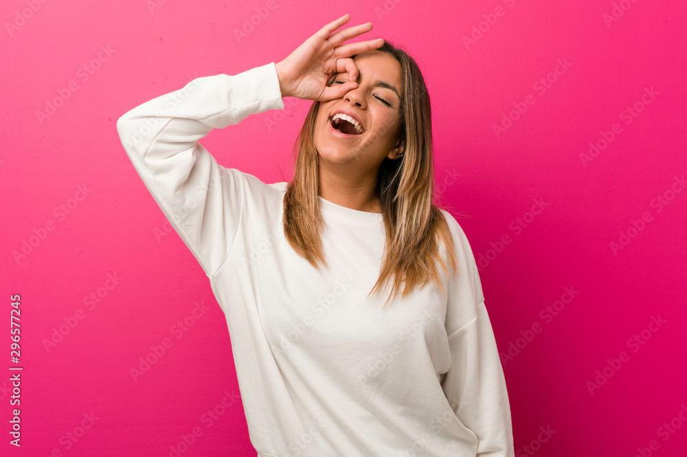 Young authentic charismatic real people woman against a wall excited keeping ok gesture on eye. Young authentic charismatic real people woman against a wall excited keeping ok gesture on eye.