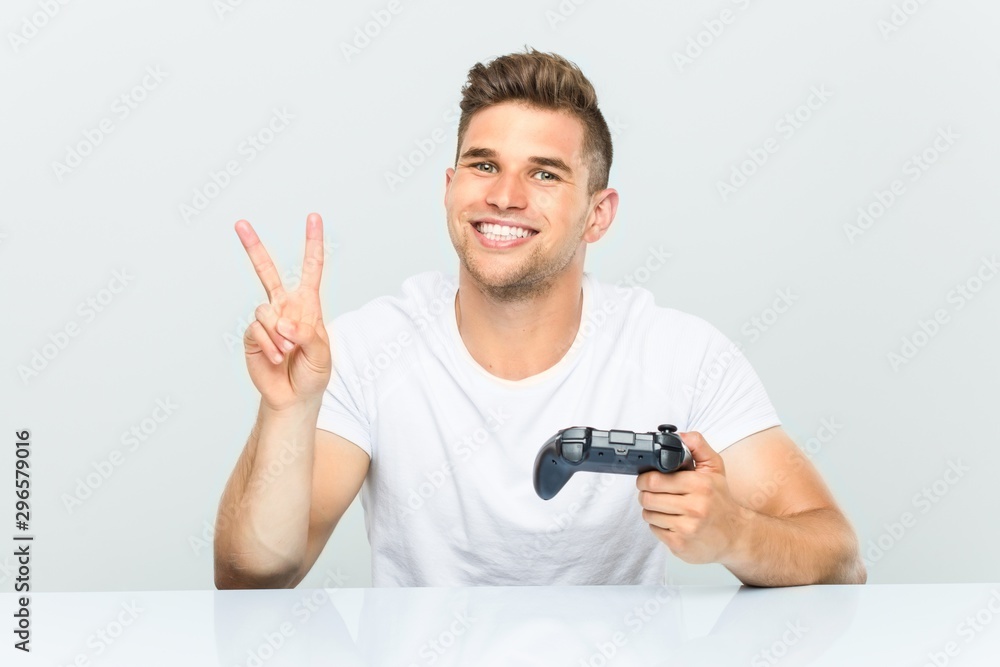 Young man holding a game controller showing number two with fingers. Young man holding a game controller showing number two with fingers.