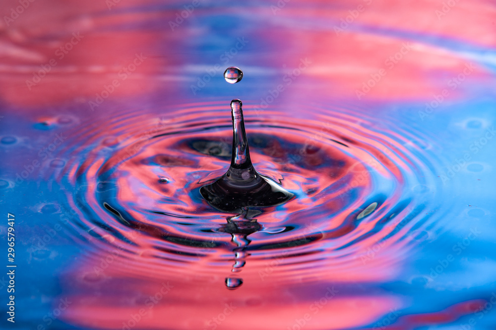 Single water drop at top of splash. Vibrant red and blue colors, high speed water drop photography