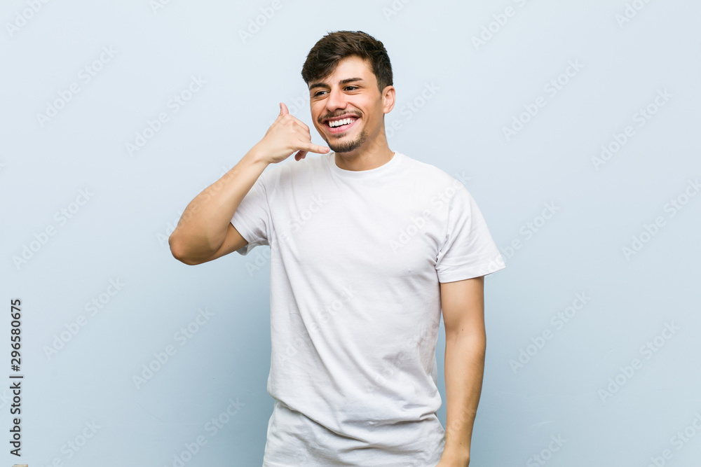 Young caucasian man wearing a white tshirt showing a mobile phone call gesture with fingers. Young caucasian man wearing a white tshirt showing a mobile phone call gesture with fingers.