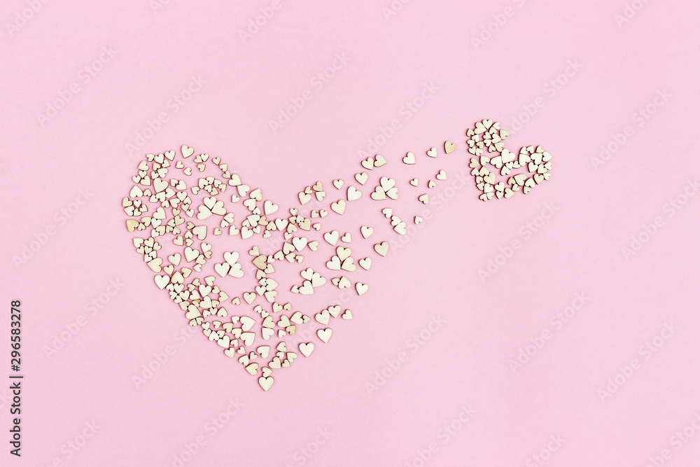 Small heart emerges from large one. Birth of new love. Concept of love. Many small wooden hearts on pink background. Flat lay. - obrazy, fototapety, plakaty 