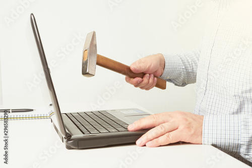 The man raised a hammer over the computer, man in the shirt wants to break the laptop. The concept of fatigue from work photo