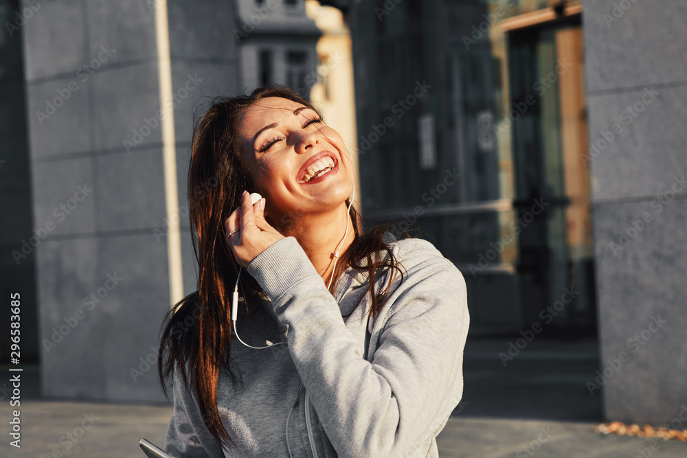 Young woman in gray hoodie enjoys music via earphones on the street Young woman in gray hoodie enjoys music via earphones on the street