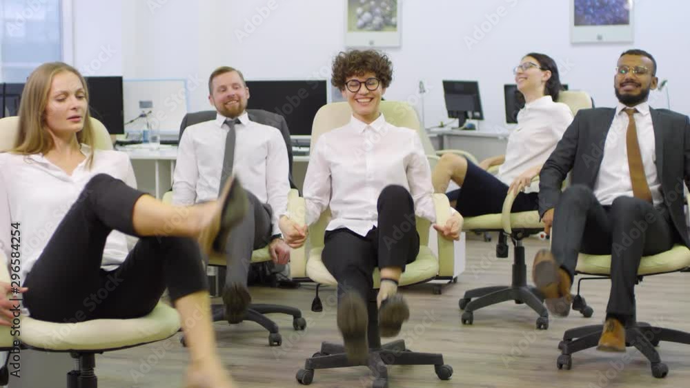 Wide shot of team of diverse businesspeople sitting on office chairs and warming up their legs together and then relaxing Wide shot of team of diverse businesspeople sitting on office chairs and warming up their legs together and then relaxing