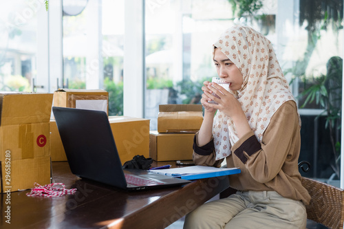 Thai young muslim business woman wearing hijab sitting at table work place drinking water. Stay hydrated.