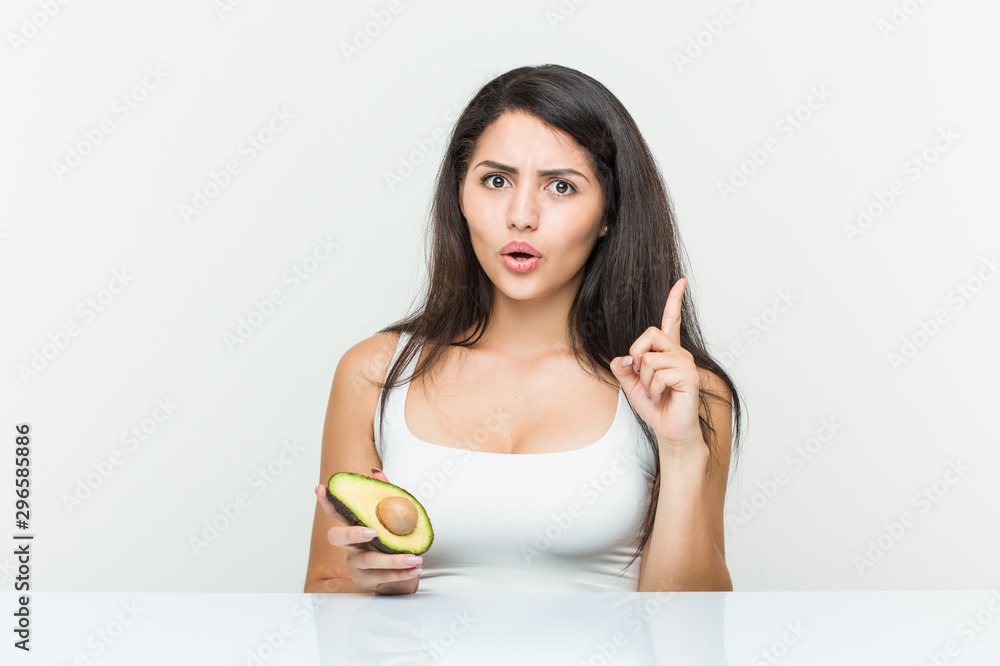 Young hispanic woman holding an avocado having some great idea, concept of creativity. Young hispanic woman holding an avocado having some great idea, concept of creativity.
