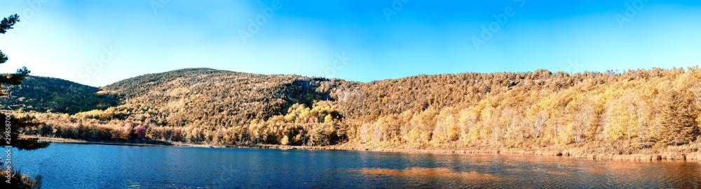 Panoramic aerial view of lake and trees in autumn foliage seaon against blue sky Panoramic aerial view of lake and trees in autumn foliage seaon against blue sky
