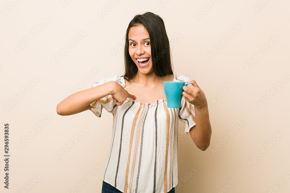 Young hispanic woman holding a cup surprised pointing at himself, smiling broadly. Young hispanic woman holding a cup surprised pointing at himself, smiling broadly.