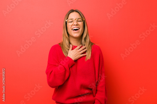 Young authentic charismatic real people woman against a wall laughs out loudly keeping hand on chest. © Asier