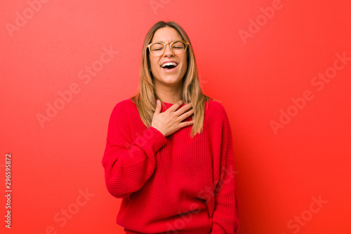 Young authentic charismatic real people woman against a wall laughs out loudly keeping hand on chest.