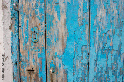 Part of an old wooden door with peeling blue paint and a keyhole