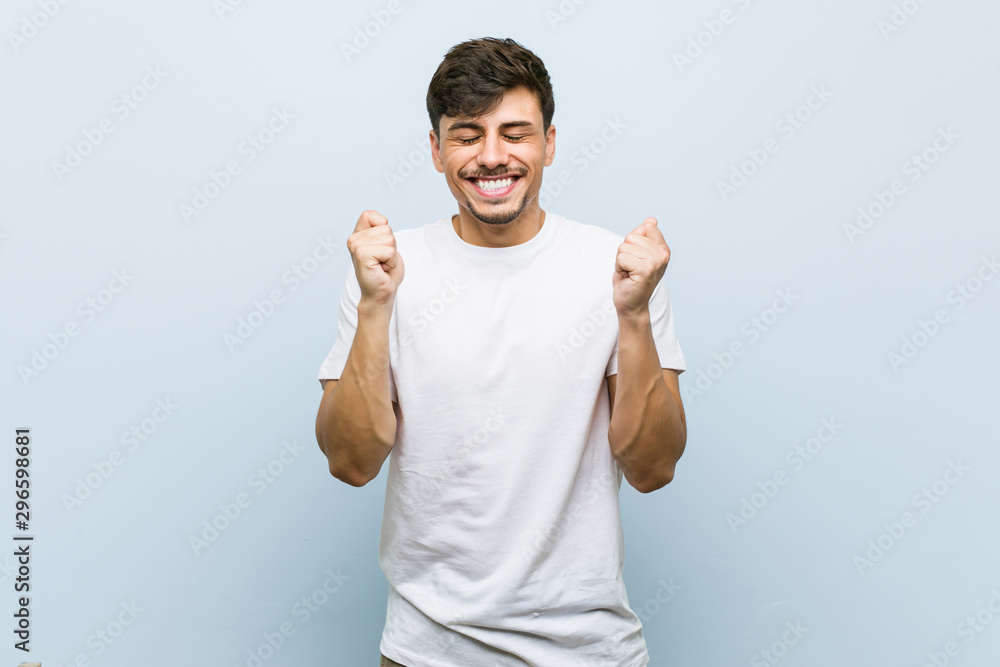 Fototapeta premium Young caucasian man wearing a white tshirt raising fist, feeling happy and successful. Victory concept.