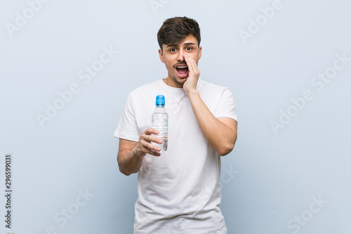 Young hispanic man holding a water bottle shouting excited to front.