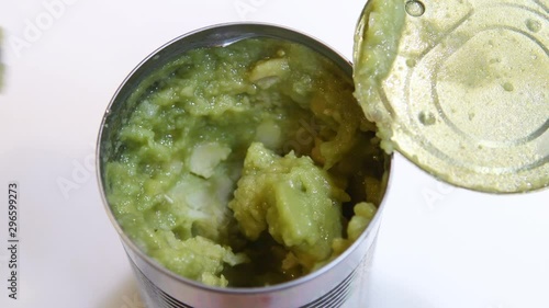 Close up of spoon appearing with open tin of British mushy peas. Taking spoonful of mushy peas out of aluminum can. Video of food preparation. Comfort food.