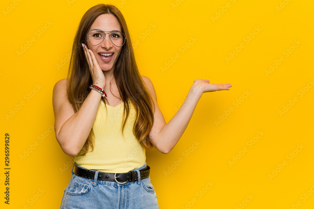 Young redhead ginger woman with freckless holds copy space on a palm, keep hand over cheek. Amazed and delighted. Young redhead ginger woman with freckless holds copy space on a palm, keep hand over cheek. Amazed and delighted.
