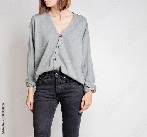 Young woman wearing simple outfit with grey button-up cardigan and black trousers isolated on light grey background. Copy space