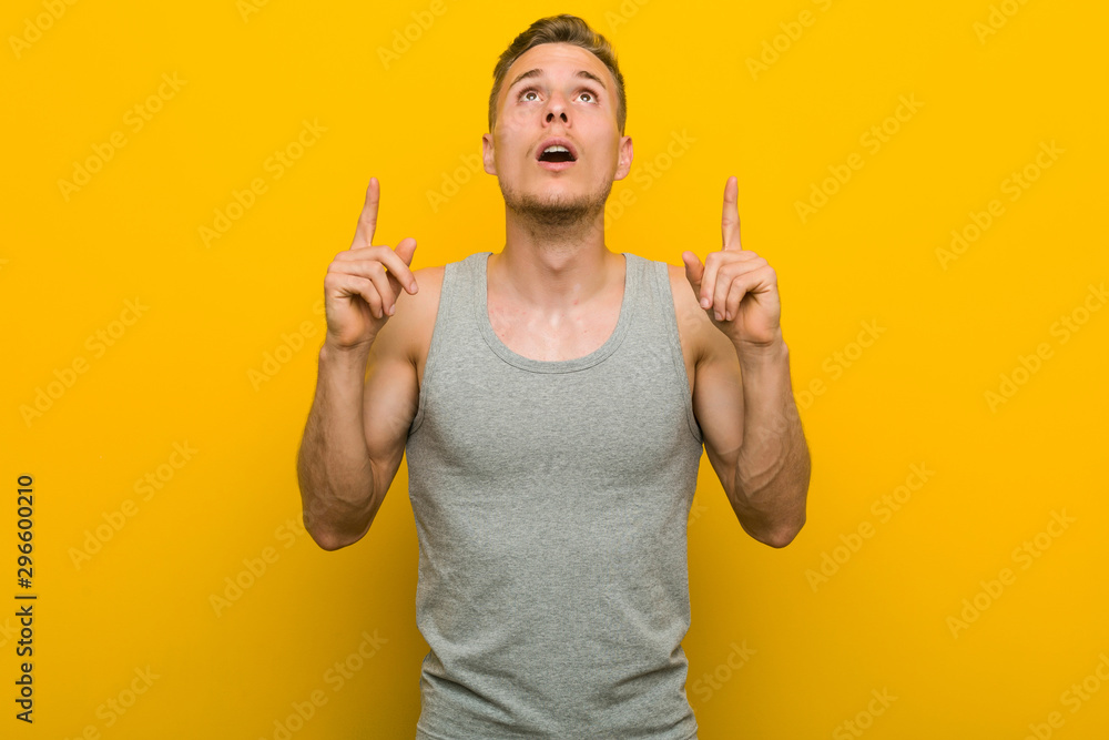 Young caucasian sport man pointing upside with opened mouth. Young caucasian sport man pointing upside with opened mouth.