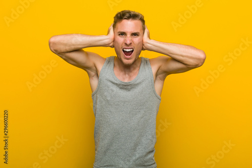 Young caucasian sport man covering ears with hands trying not to hear too loud sound. © Asier
