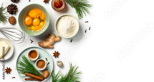 Ingredients for baking Christmas ginger cookies on a white background, copy space. Flour, eggs, ginger, spices, butter, green pine branches and cones on the table, flat lay. Winter food background.