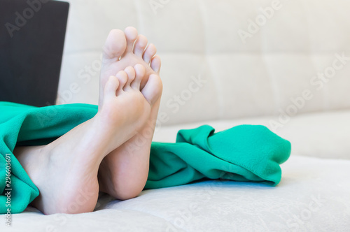 girl sitting at home on the sofa with a laptop legs stick out from under the plaid. social networks, communication, addiction.