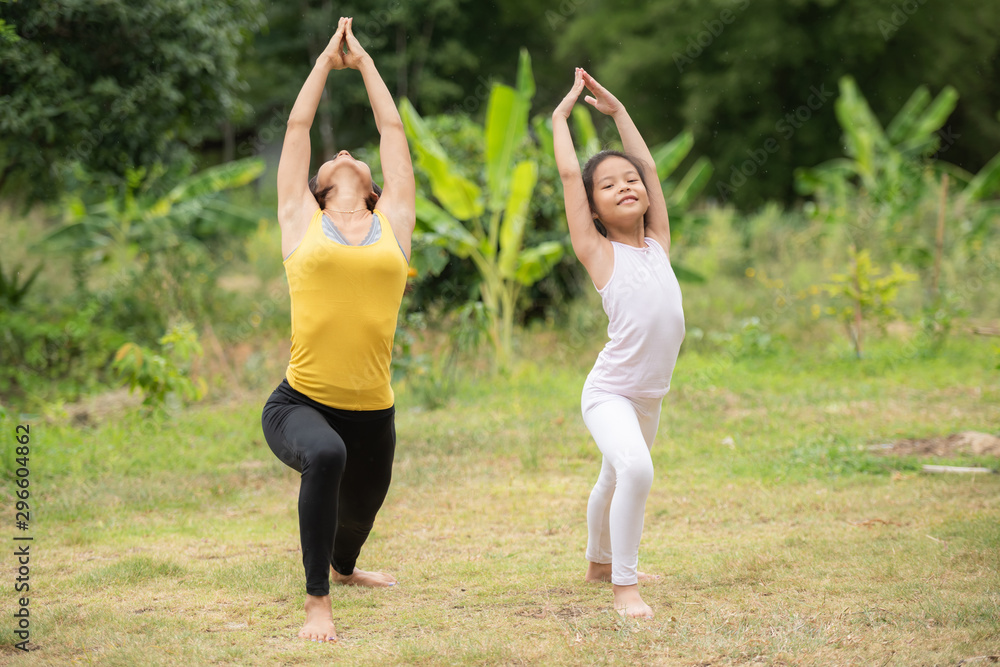 asia Mother and daughter doing yoga exercises on grass in the park at the day time. People having fun outdoors. Concept of friendly family and of summer vacation. asia Mother and daughter doing yoga exercises on grass in the park at the day time. People having fun outdoors. Concept of friendly family and of summer vacation.