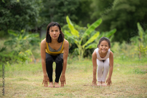 asia Mother and daughter doing yoga exercises on grass in the park at the day time. People having fun outdoors. Concept of friendly family and of summer vacation.