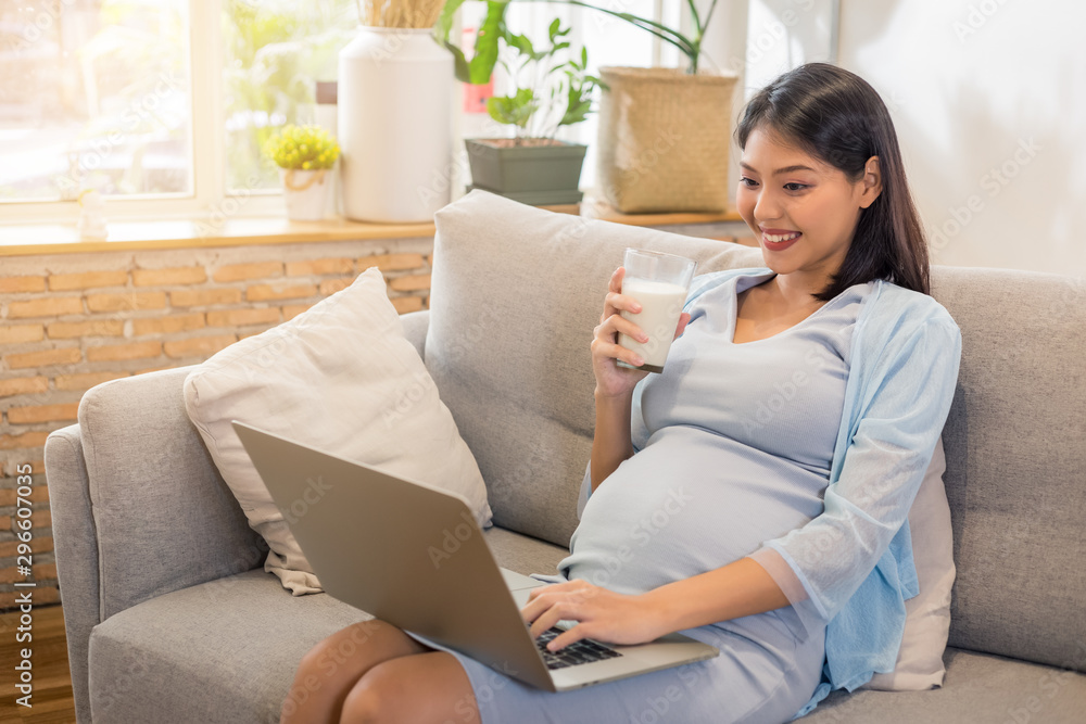 Young beauty happy Asian pregnant woman holding glass of milk using computer. Young beauty happy Asian pregnant woman holding glass of milk using computer.