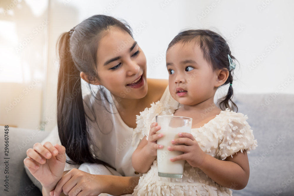 Young happy Asian mother and daughter coloring together at home with art tools and a glass of milk.