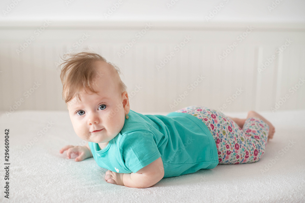 Adorable Caucasian baby girl with blue eyes trying to stand up and walk, looking at the camera calmly with a smile; cute baby facial expressions and learning steps or motherhood and family concepts Adorable Caucasian baby girl with blue eyes trying to stand up and walk, looking at the camera calmly with a smile; cute baby facial expressions and learning steps or motherhood and family concepts