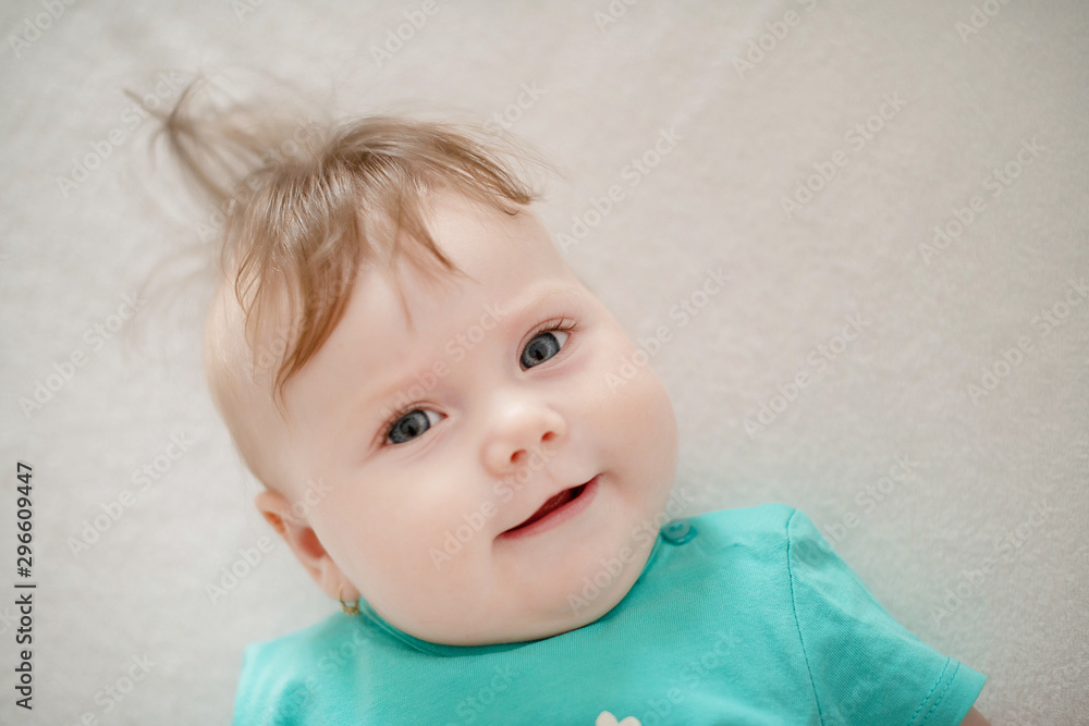 Naklejka premium Portrait of adorable baby girl with blue eyes and cute hair looking at the camera calmly with a smile; cute baby facial expressions and learning steps or motherhood and family and fertility concepts