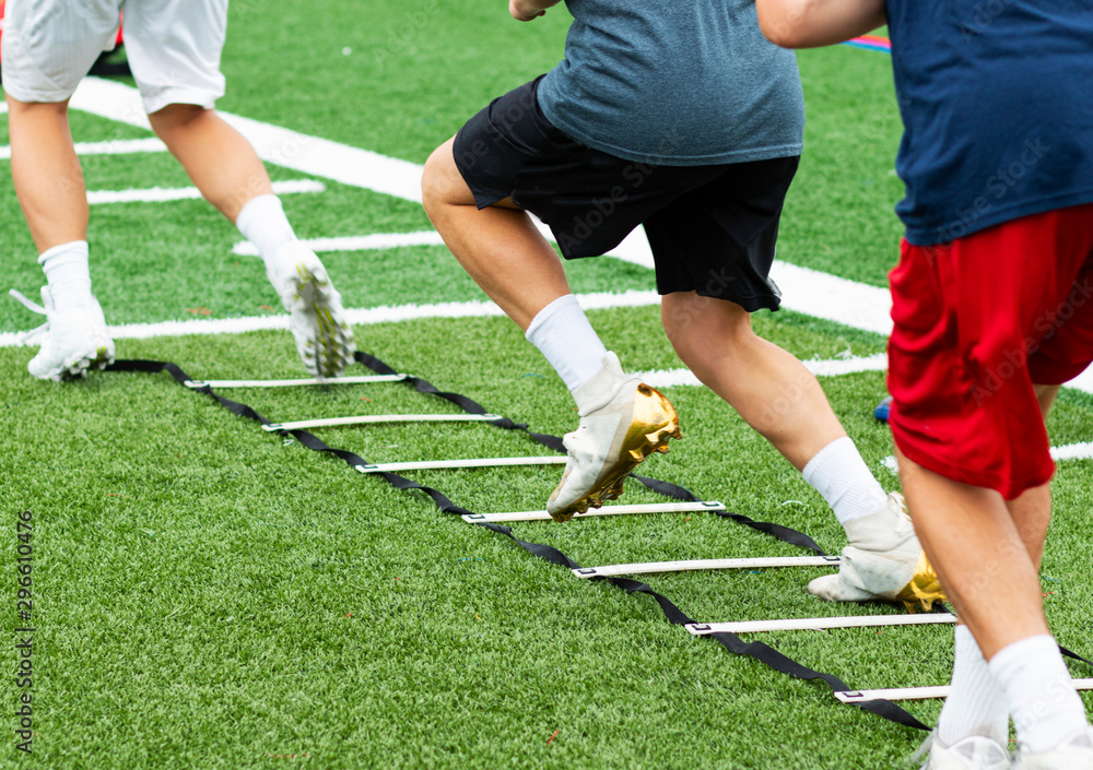 Three athletes in cleats doing ladder foot drills on turf field Stock