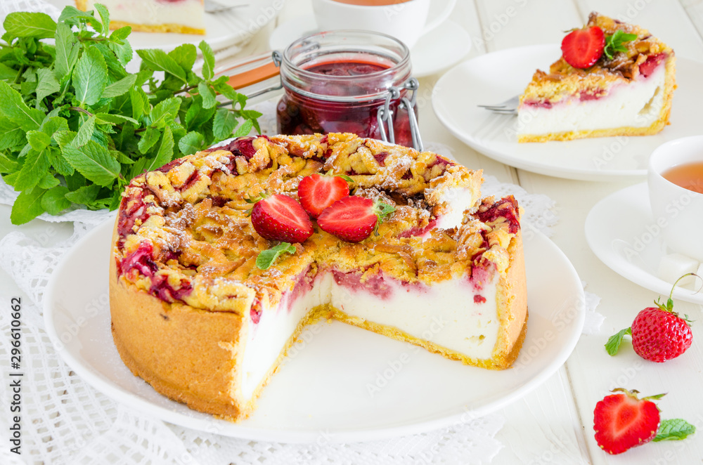 Baked creamy cheesecake with strawberries and crispy shtrezel on a plate on a white wooden background with a cup of tea. Baked creamy cheesecake with strawberries and crispy shtrezel on a plate on a white wooden background with a cup of tea.
