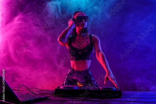 Young sexy woman dj in bra and sunglasses playing music. Headphones and dj mixer on table. Colorful Smoke on background photo