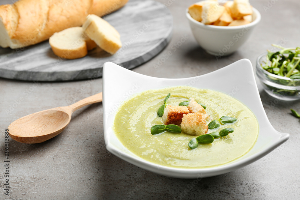 Bowl of broccoli cream soup with croutons and microgreens served on grey table