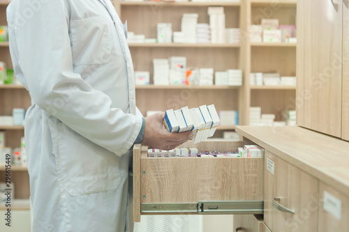 the pharmacist takes a package of medicine from a box in a pharmacy