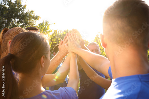 Group of volunteers joining hands together outdoors on sunny day