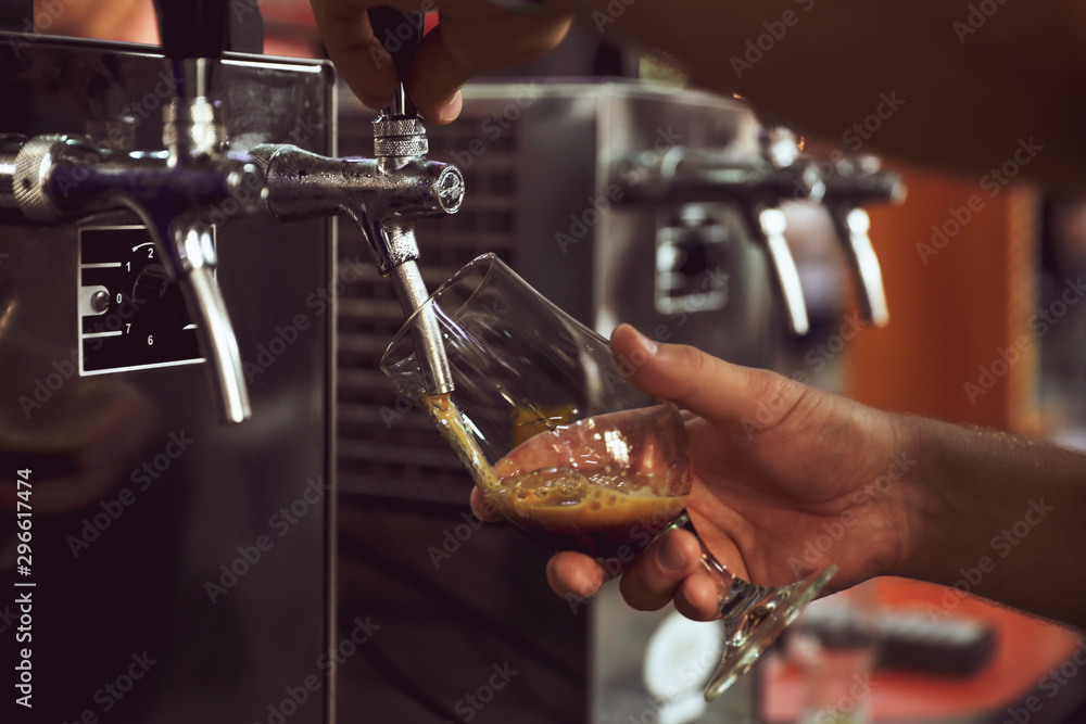 Bartender pouring beer into glass in pub, closeup