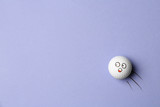 Golf ball with funny face flying on lilac background - creative image. Top view